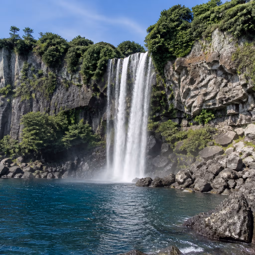 Jeongbang Waterfall front view, a 23-meter cascade dropping from a dark basalt cliff directly into the sea with mist rising along the base